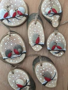 six handmade ornaments with red and grey birds hanging from strings on a wooden table