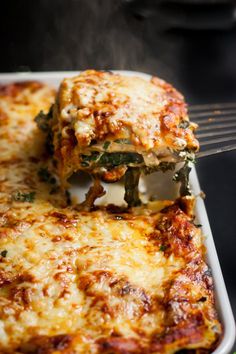 a white plate topped with lasagna covered in cheese and spinach toppings