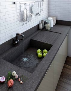 a kitchen sink with two green apples in the water and some vegetables on the counter