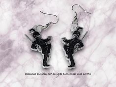 a pair of black and white earrings featuring a skeleton holding a baseball bat on a marble background