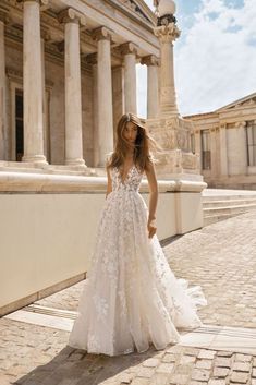 a woman in a wedding dress standing on the side of a building with columns behind her