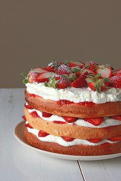 a cake with strawberries and whipped cream on top sitting on a white wooden table