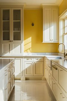 an empty kitchen with yellow walls and white cupboards on either side of the sink