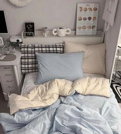 an unmade bed with blue sheets and pillows in a small room next to a desk