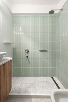 a bathroom with green tiled walls and white fixtures, including a shower head in the corner