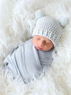 a newborn baby wearing a knitted hat and sleeping on a white fluffy blanket with his eyes closed