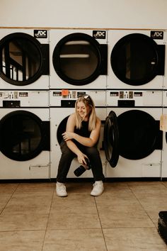 a woman sitting on the floor in front of washing machines