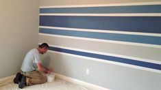 a man painting a wall with blue and white stripes on the walls in an empty room