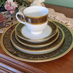 a stack of white and gold plates on top of a wooden table with flowers in the background