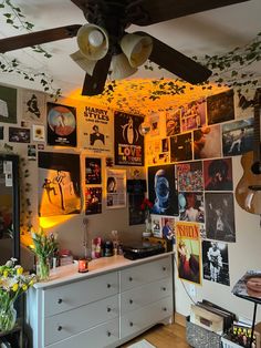 a living room filled with lots of pictures and plants on the wall next to a dresser