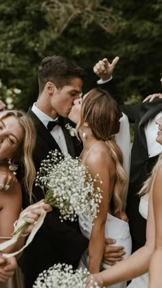 a group of people standing next to each other with flowers in their hands and one woman kissing the man's cheek