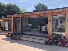 a small wooden building with lots of windows and flowers in the front yard, along with potted plants on either side