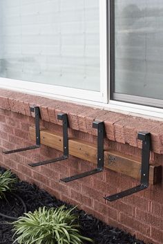 three coat hooks are attached to the side of a brick building with plants in front