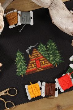 a cross stitch on black fabric of a cabin in the woods surrounded by pine trees. Cabin Cross Stitch, Cozy Cabin In The Woods, Beginner Cross Stitch, Frame House, A Frame House, Cabin In The Woods, Cozy Cabin, Fall Design