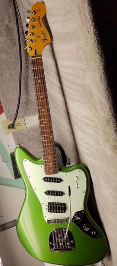 a green electric guitar sitting on top of a white bed next to a charger