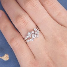 a woman's hand with a diamond ring on top of her finger and flowers in the background