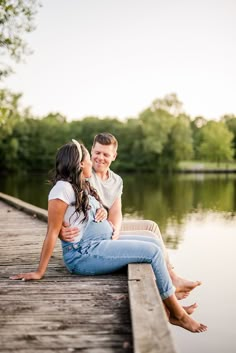 a man and woman sitting on a dock next to the water looking at each other