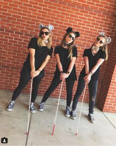 three girls dressed up as cats and holding canes in front of a brick wall