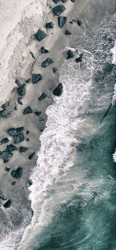 an aerial view of the ocean with rocks and waves crashing on the beach, taken from above