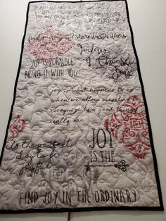 a quilt with writing on it hanging from the wall in front of a white wall