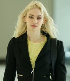 a woman with blonde hair wearing a black blazer and yellow shirt is walking down the street