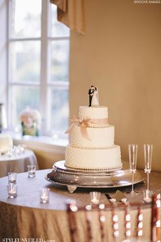 a white wedding cake sitting on top of a table next to wine glasses and candles