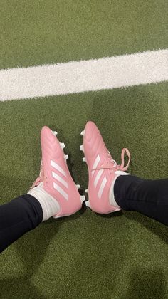 the feet of a person wearing pink tennis shoes on a green grass covered soccer field