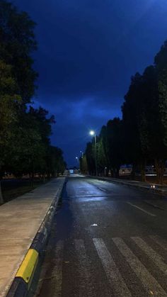 an empty street at night with the lights on and dark clouds in the sky above