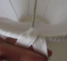 a hand holding a piece of white cloth with a needle sticking out of it's end