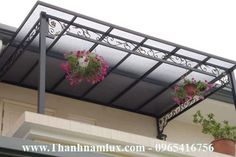 two hanging flower pots with pink flowers in them on the side of a building under a metal awning