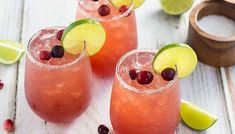 three glasses filled with drinks and garnished with limes, cranberries, and cherries