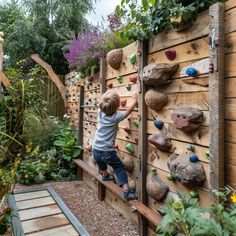 a young boy climbing up the side of a wooden wall with rocks on it in a garden