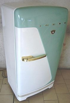 an old fashioned refrigerator sitting on the floor in front of a white wall and tiled floor