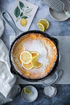 a lemon cake with powdered sugar on top and sliced lemons in the background