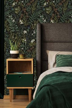 a bedroom with green wallpaper and a bed in front of the nightstand has a potted plant on it