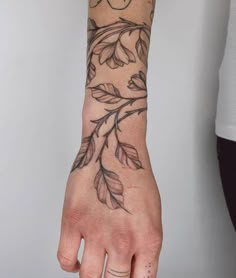 a person's hand with tattoos on it, and the wrist is covered in leaves