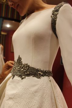 a woman wearing a white dress with silver beading on the waist and long sleeves