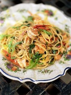 a white plate topped with pasta and shrimp on top of a wooden table next to a grill