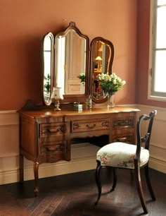 an antique desk with mirror, chair and flower arrangement