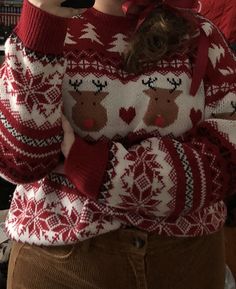 a woman wearing a red and white sweater with reindeers on it is taking a selfie