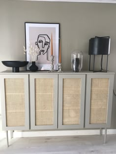 a sideboard with wicker doors in a living room next to a lamp and pictures