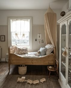 a bed sitting next to a window in a room with wooden floors and white walls