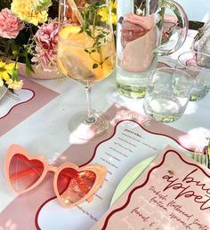 a table topped with glasses and flowers next to a card that says happy valentine's day