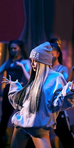 a woman with long hair wearing a beanie and blue sweatshirt in front of dancers