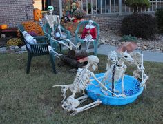 skeleton statues sitting in the grass near lawn chairs and pumpkins with fake skeletons on them