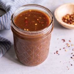 a glass jar filled with sauce next to a wooden spoon and striped napkin on a white surface