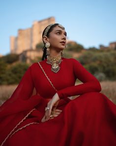 a woman in a red dress sitting on the ground with a castle in the background