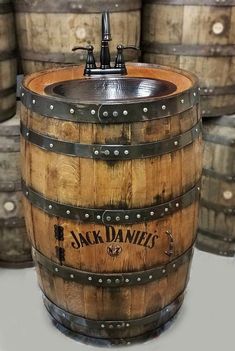 a wooden barrel sink sitting in front of some wine casks on the floor and under it is a faucet that reads jack daniels