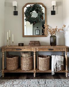 a console table with baskets under a mirror and candles on the wall next to it