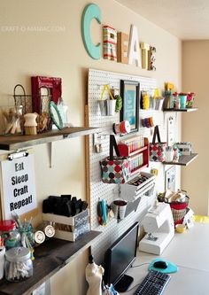 a computer on a desk in front of a shelf filled with craft supplies and other items